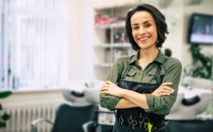 Hair school instructor in the salon smiling at the camera with folded arms.