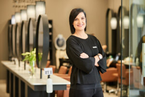 Hair school instructor in the salon smiling at the camera with folded arms.