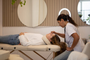 An esthetician applying a facial to a client who laying on a table.