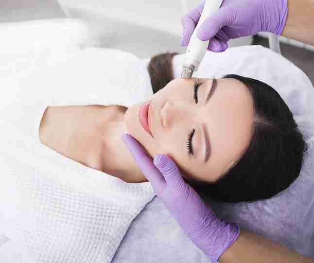 an esthetician applying a facial to a client who is laying on a table.