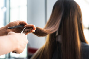 A hairdresser trimming the ends of a client with brunette hair.