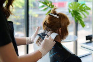A hairdresser touching up a clients roots who has dyed red hair.