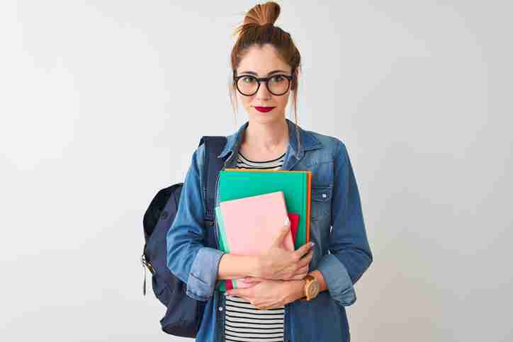 A student with glasses is standing and looking at the camera with their notebooks and backpack.