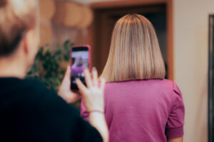 A women with her hair freshly cut to her shoulders is facing away from the camera with another women taking a picture of her hair.