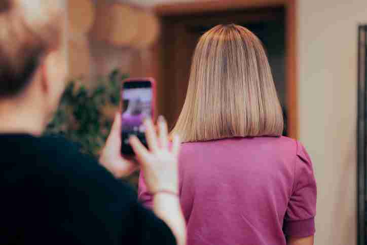 A women with her hair freshly cut to her shoulders is facing away from the camera with another women taking a picture of her hair.