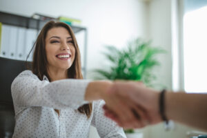 A graduate sitting in an office shaking an interviewers hand and smiling at them.