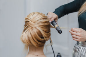 A women curling and styling another women's blonde hair in a updo.