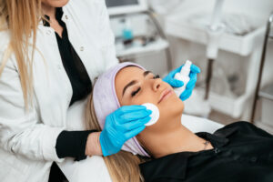 An esthetician applying a facial to a women lying on a table.