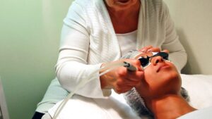 An esthetician is applying a facial to a client's face. The client is wearing eye protection.