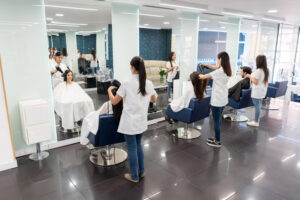 3 hairdressers in a salon blow drying, cutting, and styling their client's hair.