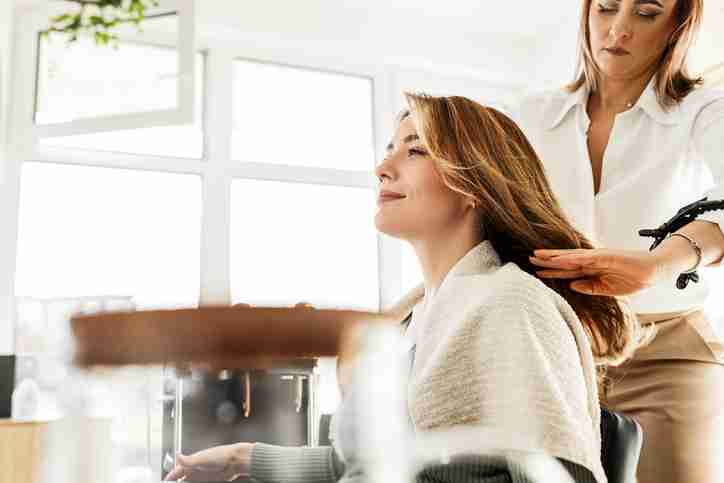A hairdresser dry cutting a clients hair in a salon booth.