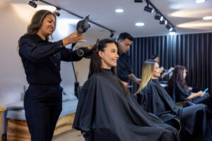 3 hairdressers in a salon blow drying, cutting, and styling their client's hair.