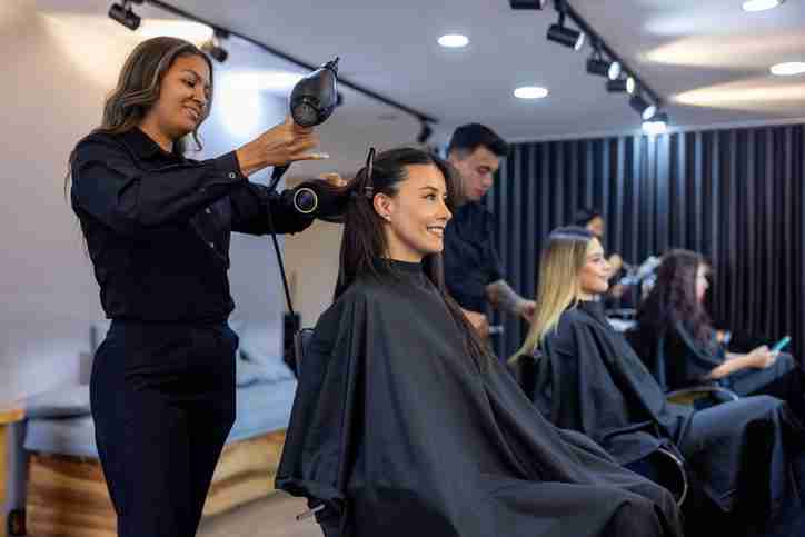 3 hairdressers in a salon blow drying, cutting, and styling their client's hair.