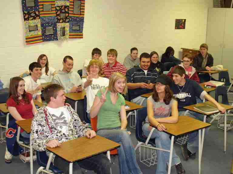 A classroom of students from the early 200s smiling at the camera and sitting in their chairs.