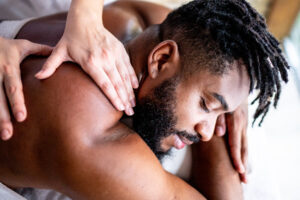 A man laying on a massage table with a massage therapist massaging his shoulders.