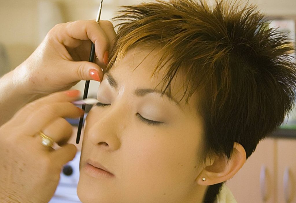 Student applying eye makeup to a client in a professional cosmetology training setting.