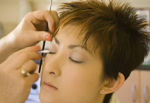 Student applying eye makeup to a client in a professional cosmetology training setting.