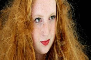 Portrait of a girl with vibrant curly red hair, smiling and looking into the camera.