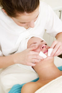 A esthetician applies a facial to a client who is lying on the table.