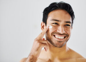 A profile image of a man applying face cream to his cheek.