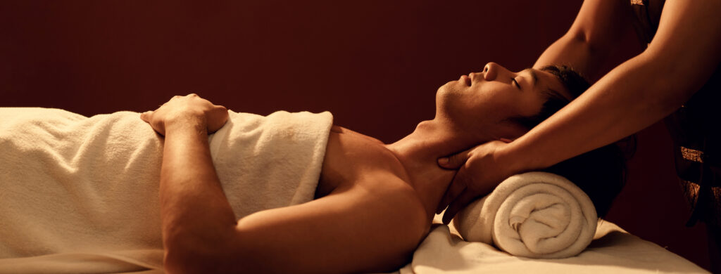 A side profile of a man on a massage table having a massage therapist massage his shoulders.