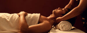 A side profile of a man on a massage table having a massage therapist massage his shoulders.