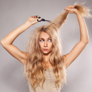 A woman with long blonde hair holding scissors to a chunk of her hair.