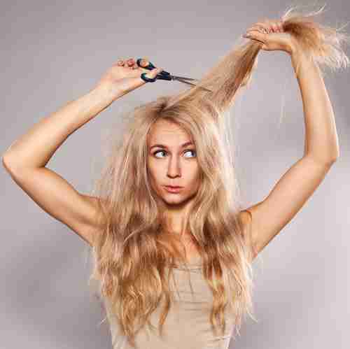 A woman with long blonde hair holding scissors to a chunk of her hair.