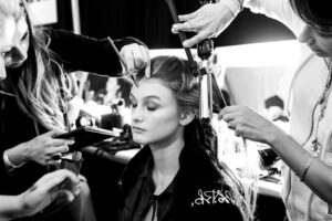 3 cosmetologists doing a women's hair and makeup in a dressing room.