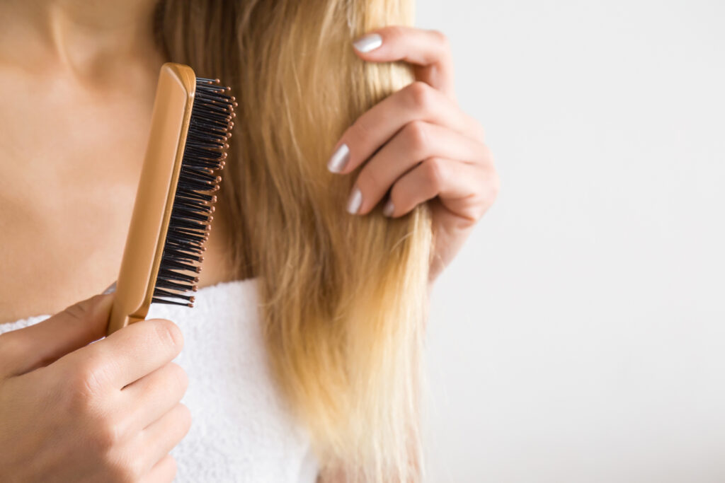 A closeup of a women with blonde hair brushing the ends of her hair.