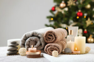 Massage items including towels, candles, stones, are all set on a massage table. There is a christmas tree in the background.
