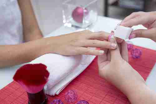 A nail tech is filing a client's French manicure.