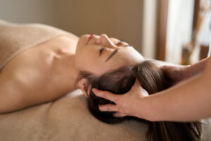 A woman lying on a massage table with a massage therapist massaging her scalp.