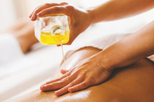 A close-up of a massage therapist pouring and applying massage oil to a client's back.