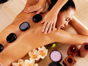 A woman lying on a massage table with a massage therapist massaging her back. She has hot stones on her back as well.
