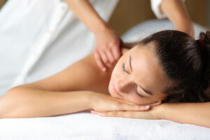 A woman lying on a massage table with a massage therapist massaging her back.