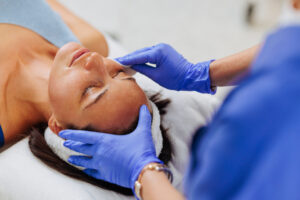 An esthetician wearing blue gloves applying a treatment to a client's face.