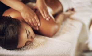 A woman lying on a massage table with a massage therapist massaging her back.