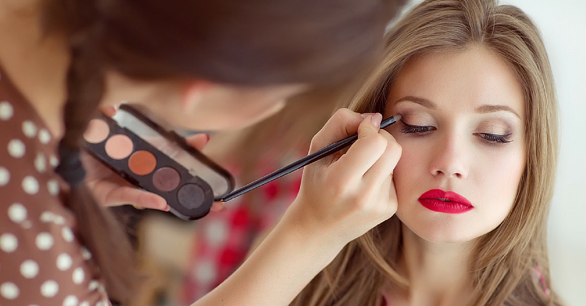 An esthetician applying glamorous makeup to a client. 