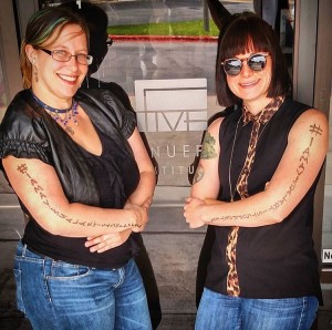 Two Avenue 5 students, posing outside the school with the hashtag I AM A VISUAL ARTIST written on their arms.