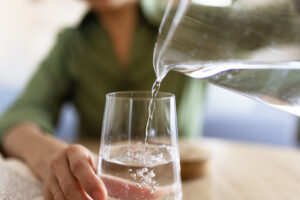 A woman in a green shirt pouring a glass of water from a pitcher.