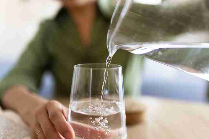 A woman in a green shirt pouring a glass of water from a pitcher.
