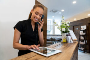 A salon worker is standing by the front desk of the salon and talking on the phone.