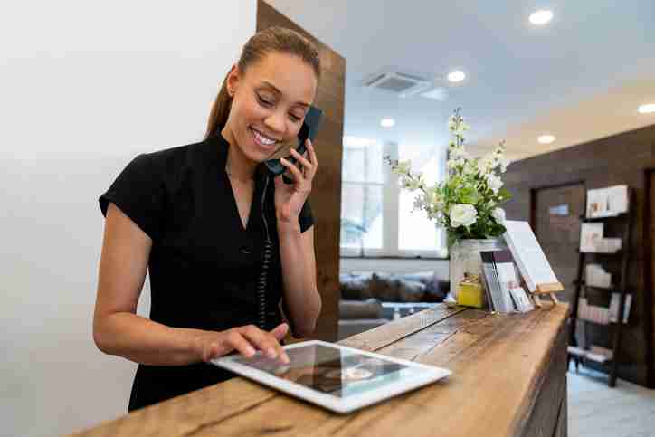 A salon worker is standing by the front desk of the salon and talking on the phone.