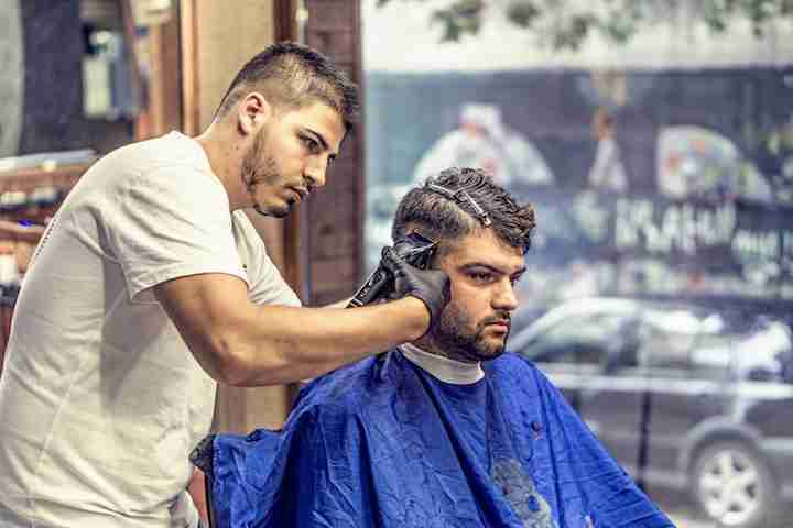 A barber student shaving the sides of a clients head.