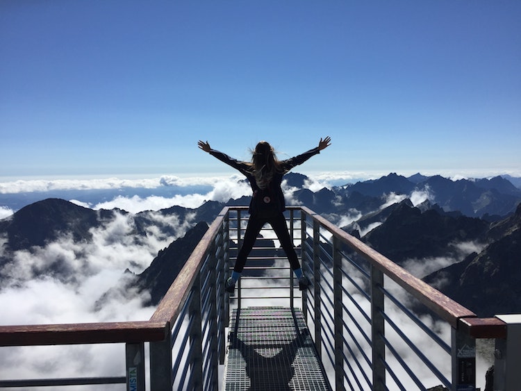 how to honor your true calling - woman stands on bridge overlooking beautiful mountains and clouds