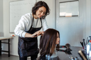 A woman practicing cutting hair on a wig.
