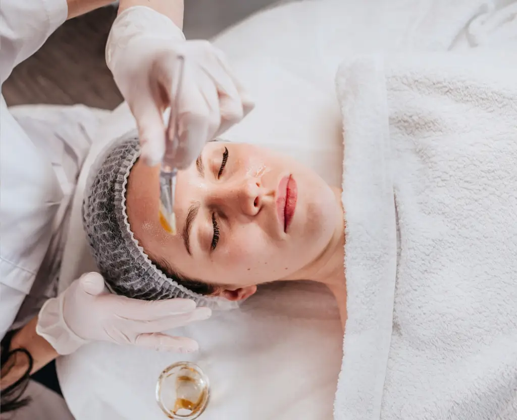 Esthetician applying a chemical peel to a client's face during a facial treatment.