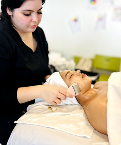 Esthetics student performing a facial treatment on a client using a face roller tool in a treatment room.