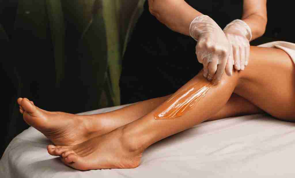 Esthetician applying warm wax to a client's leg during a hair removal treatment.